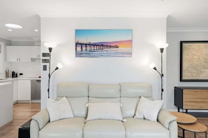 A modern living room with a sofa, a painting of a pier, and a dining area.
