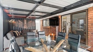 A modern interior with a glass dining table, leather chairs, a brick accent wall, and a fireplace. - Belle Escapes - Fulton Retreat (Holdfast Bay)
