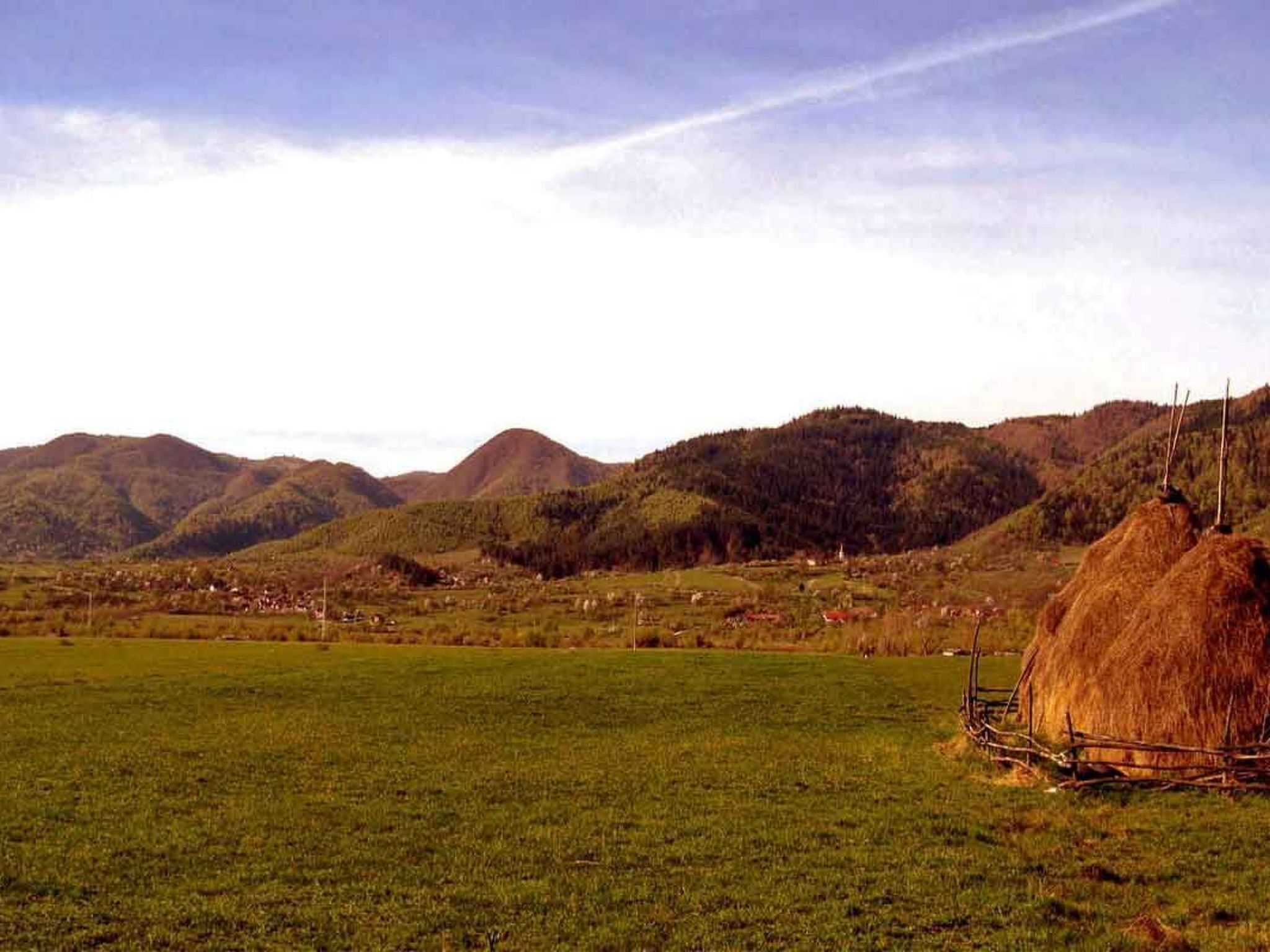 Un paysage rural avec des collines douces, un ciel dégagé et une meule de foin au premier plan.