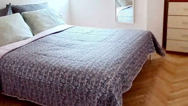 Ein Schlafzimmer mit Bett, einer Hängelampe, einem Fenster mit Vorhängen, einem Spiegel und einer Kommode.