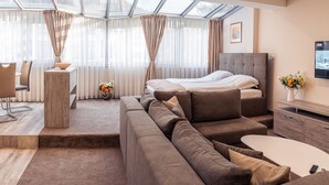 Una camera d'albergo moderna con un letto grande, un divano, una TV e un'area pranzo con tavolo e sedie.