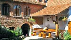 Un bâtiment traditionnel en briques, doté d’une cour en pierre, de bancs en bois et d’un espace extérieur aménagé dans un style rustique.