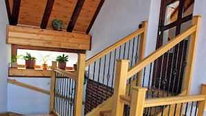 Un escalier en bois, doté d’une rampe et de balustres noires, mène à un palier où se trouve une étagère en bois sur laquelle sont disposées des plantes en pot.