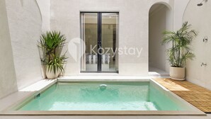 Une piscine dotée d’une terrasse carrelée, entourée de murs blancs et agrémentée de plantes en pot.