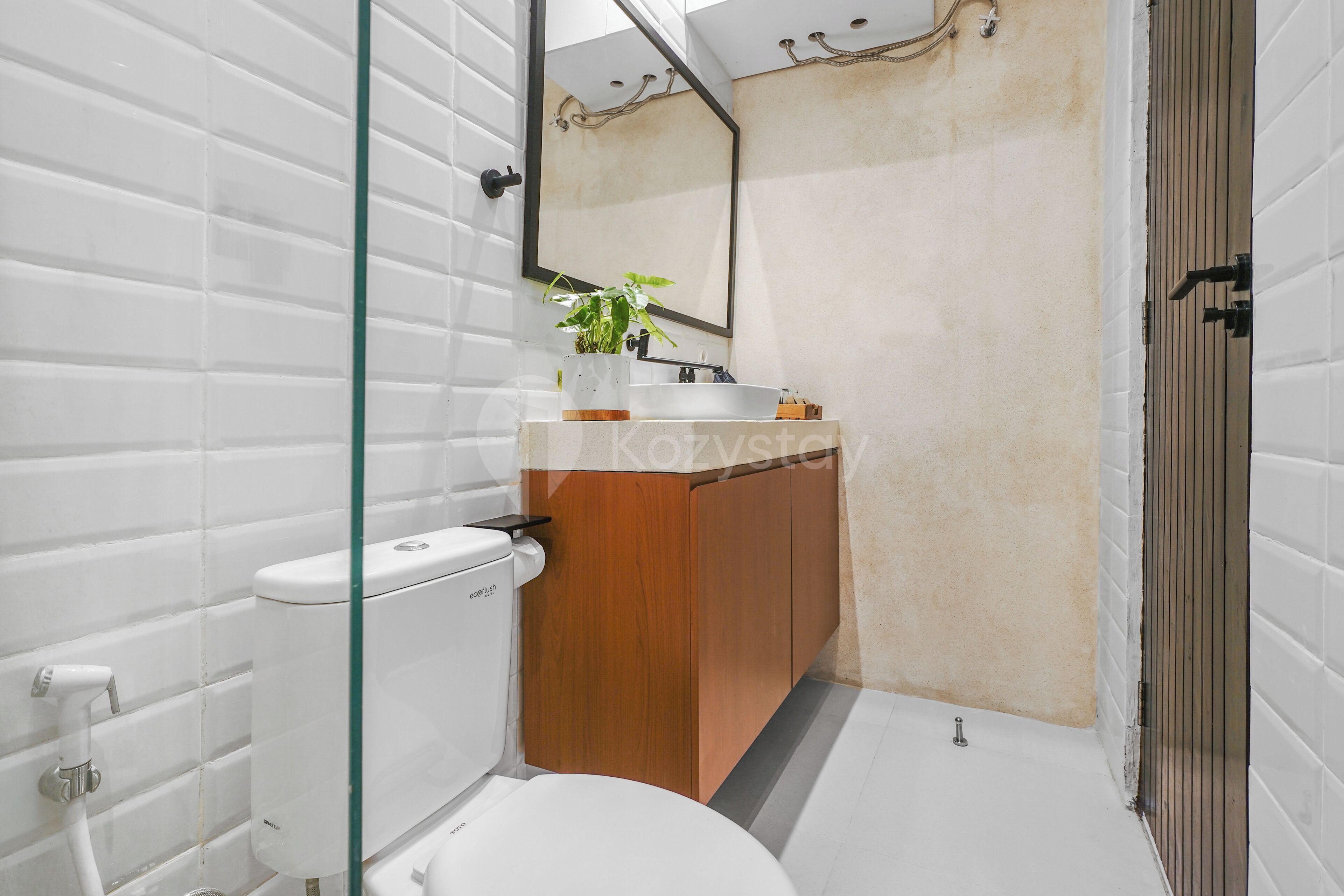 Une salle de bain moderne avec des carreaux blancs, un meuble-lavabo en bois, des toilettes blanches et une cabine de douche en verre.