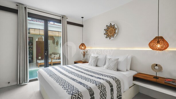 Une chambre moderne avec un grand lit, une porte-fenêtre coulissante donnant sur un balcon et deux lampes suspendues.