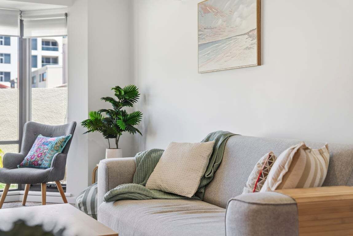 Un salón con un sofá y un sillón grises, una planta y un cuadro en la pared.