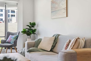 A living room with a grey sofa, a grey armchair, a plant, and a painting on the wall.