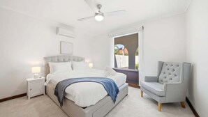 Ein Schlafzimmer mit Bett, Nachttischen, einem Sessel, einem Deckenventilator und einem Fenster mit Aussicht.