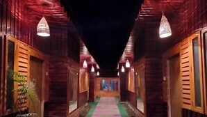 A hallway with wooden walls and a colorful carpet. There are hanging lights and plants along the sides. - Toru Nibas Eco Resort Saint Martin (Cox's Bazar)