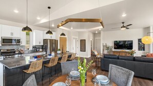 A modern kitchen with a central island, dining area with round table, and a living room with a sofa and TV. - Farmland Flat - Bozeman (Bozeman)
