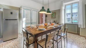 Un coin repas avec une table en bois dressée pour le repas, un réfrigérateur et une fenêtre avec des rideaux.