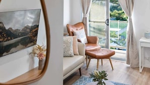 Ein modernes Wohnzimmer mit Ledersessel, Sofa und großem Fenster mit Blick auf eine Berglandschaft.