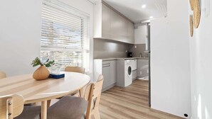 Eine kompakte Küche mit modernen Geräten, ein Essbereich mit Tisch und Stühlen sowie ein Fenster mit Jalousien.