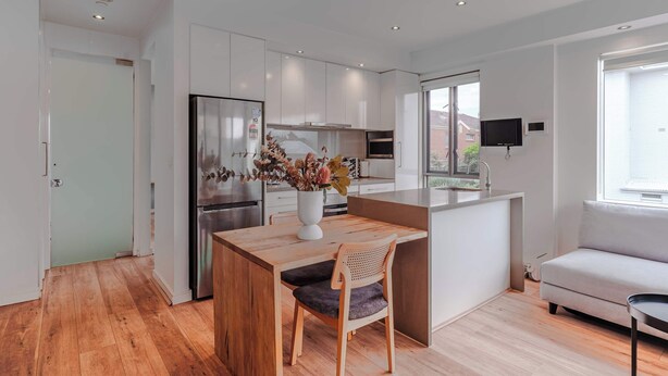 A modern kitchen with a wooden dining table, a built-in island, and a grey sofa. - Stylish 1BR Unit in Balaclava- Ideal business trip (Balaclava)