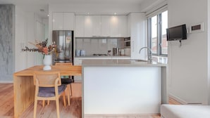 A modern kitchen with white cabinets, a stainless steel refrigerator, and a built-in oven. There's a dining area with a wooden table and chairs, and a small island with a sink. - Stylish 1BR Unit in Balaclava- Ideal business trip (Balaclava)