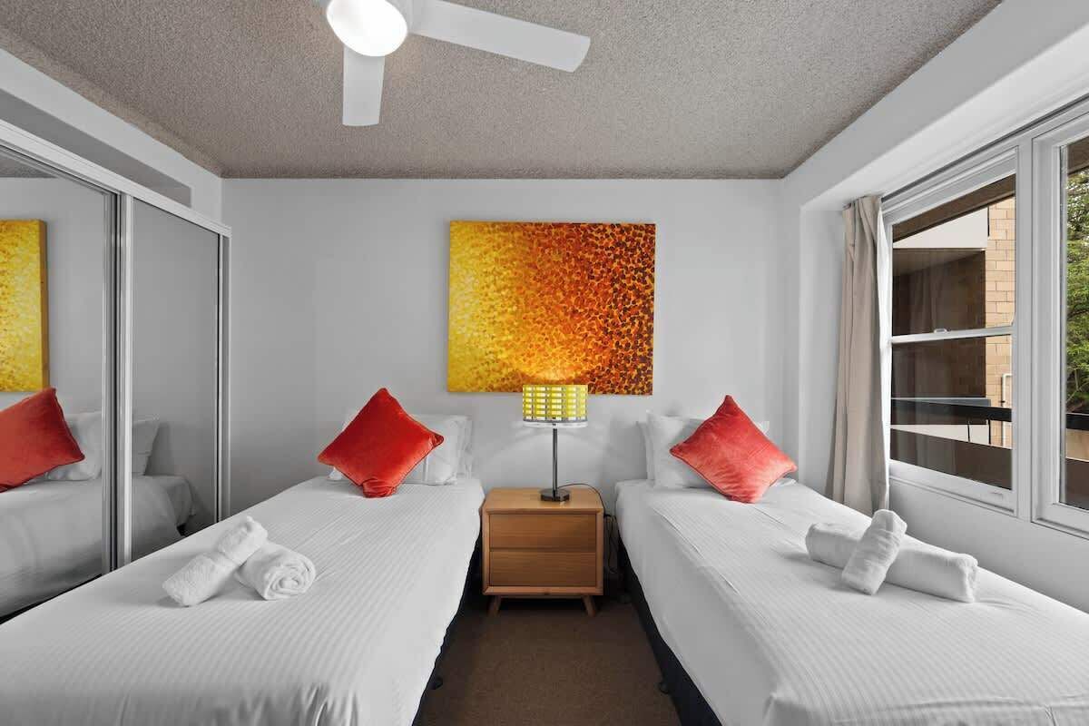 Ein Hotelzimmer mit zwei Betten, einem Deckenventilator, einem Nachttisch mit Lampe und einem großen Fenster mit Aussicht.
