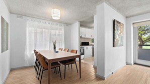 A modern kitchen with white cabinets, a wooden dining table, and a view of the outdoors. - North Adelaide View | 3BR & Free Parking (North Adelaide)