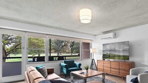 A modern living room with a sofa, armchair, coffee table, and TV. - North Adelaide View | 3BR & Free Parking (North Adelaide)