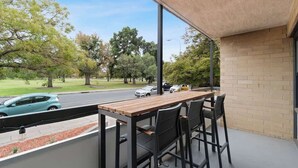 A balcony with a wooden table and chairs, overlooking a street with cars and trees. - North Adelaide View | 3BR & Free Parking (North Adelaide)