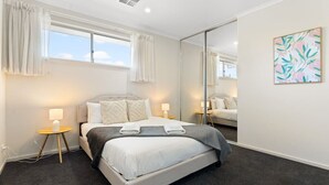 Een moderne hotelkamer met een groot bed, bedlampjes, een spiegel en een raam met gordijnen.