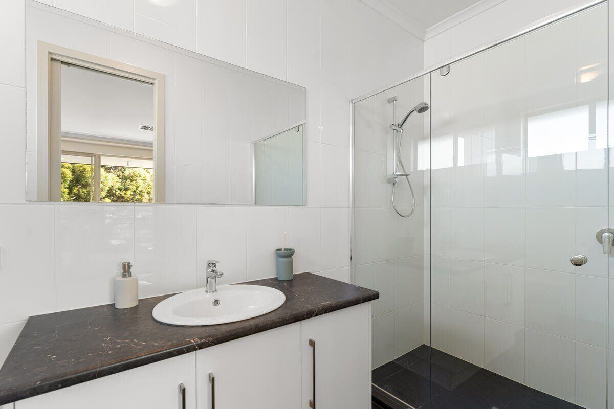 Un bagno con lavandino bianco, uno specchio e cabina doccia in vetro.