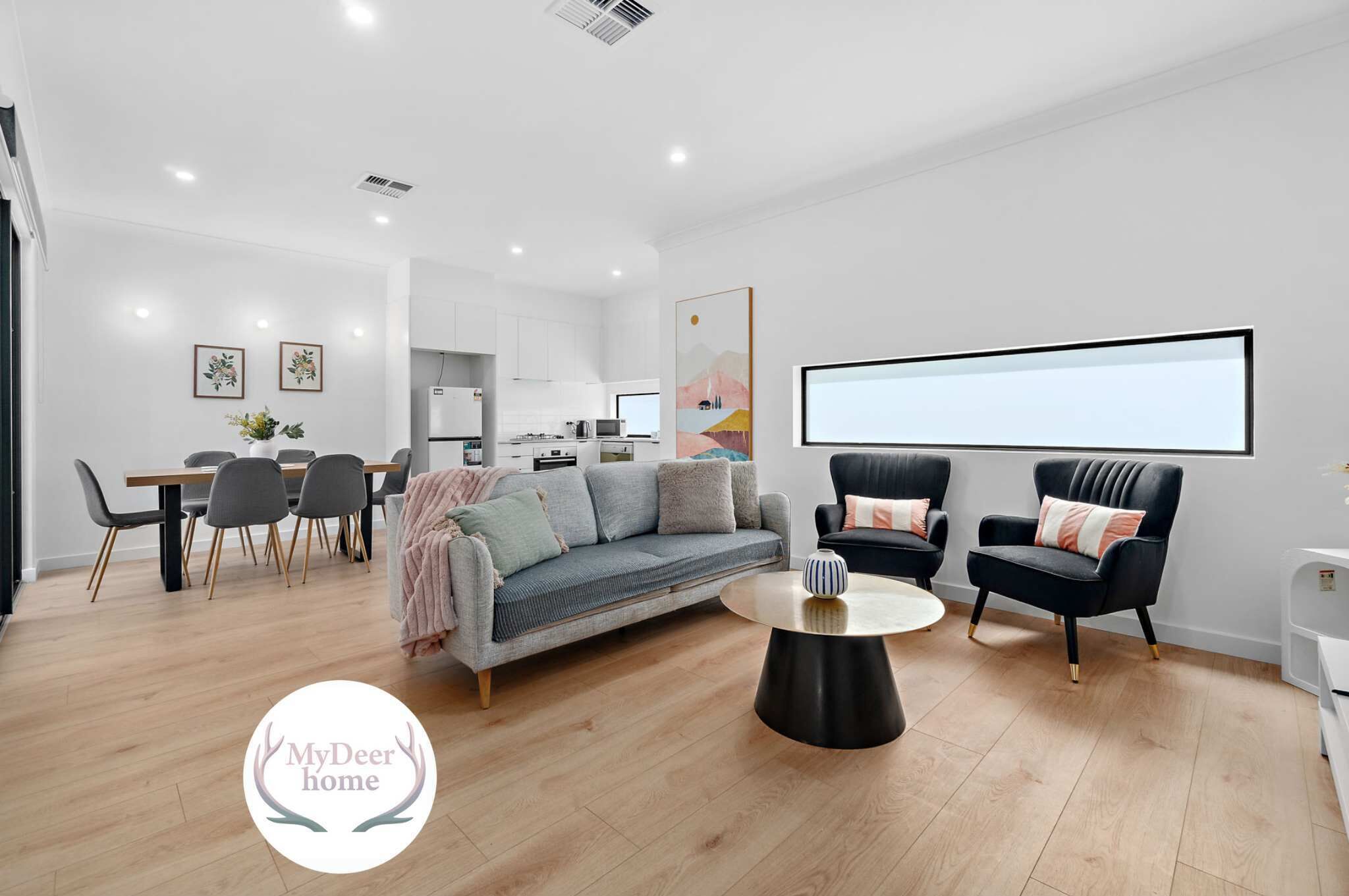 A modern living room with a sofa, two armchairs, a coffee table, and a dining area with a table and chairs.