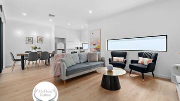 A modern living room with a sofa, two armchairs, a coffee table, and a dining area with a table and chairs.