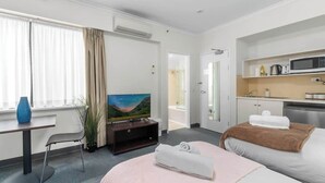 A hotel room with a bed, a TV, a desk, a chair, a bathroom, and a kitchenette.