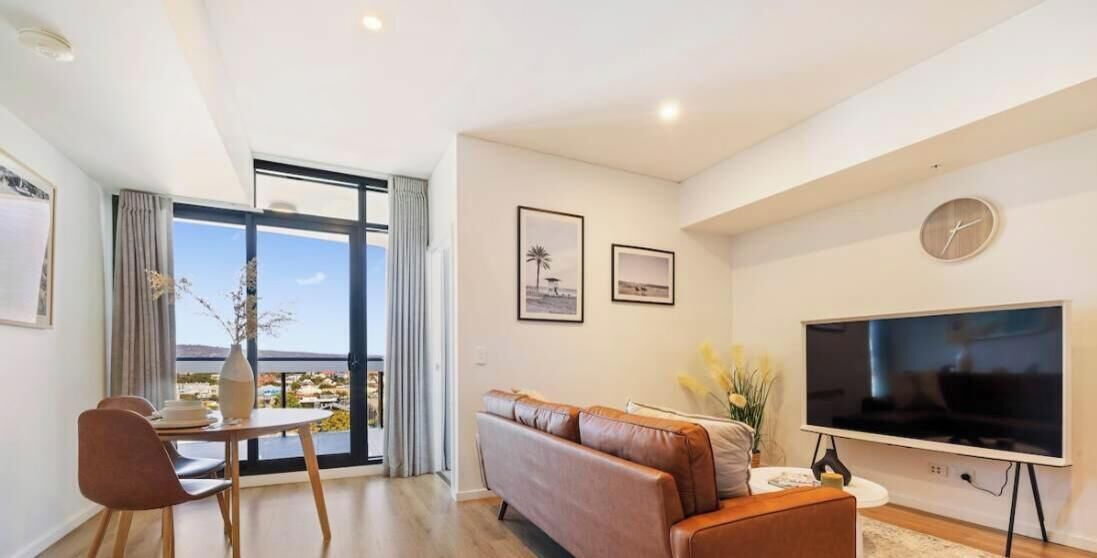 A modern living room with a sofa, a flat-screen TV, and a dining area with a table and chairs.