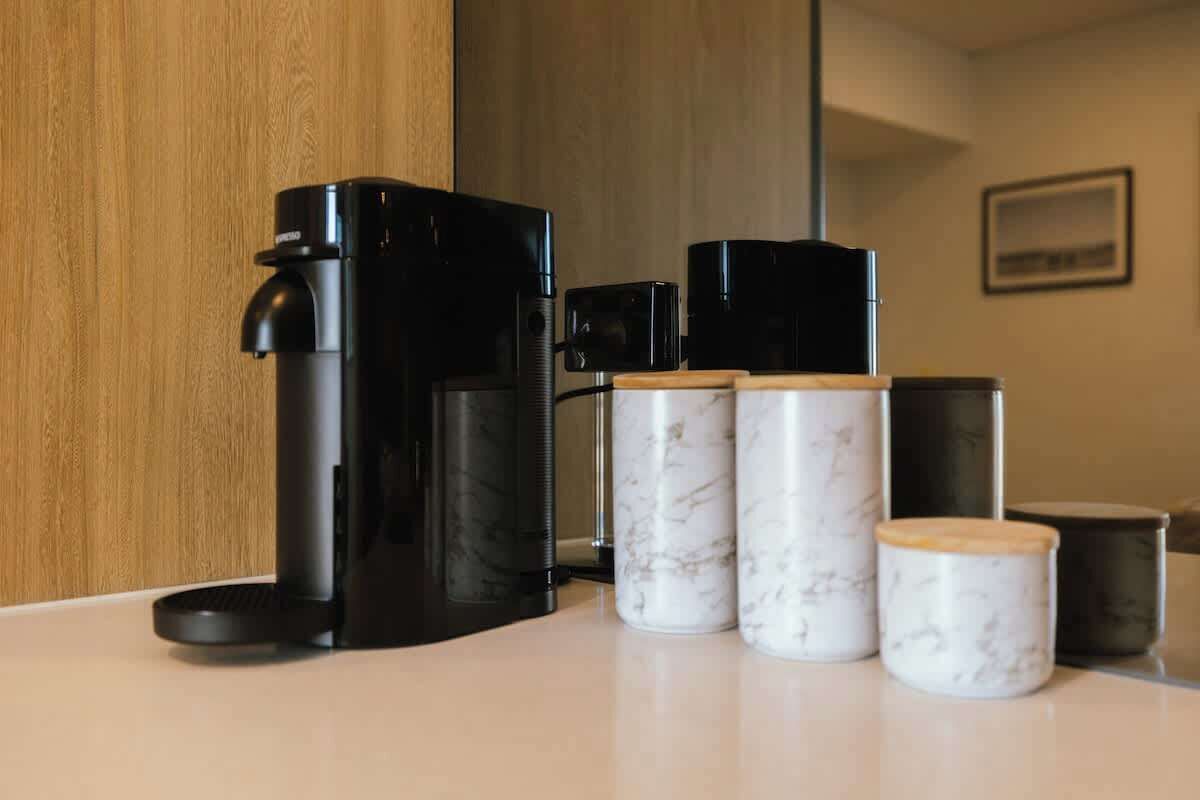 Kaffemaskine, tre beholdere med marmorlook og en træplade i et køkken.