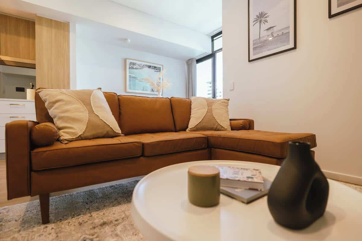 A modern living room with a brown sectional sofa, a round coffee table, and a black vase.