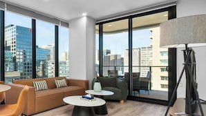 A modern living room with a sofa, two round tables, a lamp, and a view of the cityscape through large windows. - CBD VTA Apartment | Free Parking | Walk Everywhere (Adelaide)