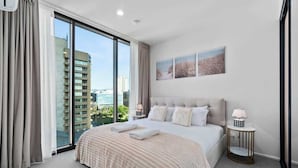A modern hotel room with a large bed, a view of the city, and a small side table with a lamp. - CBD VTA Apartment | Free Parking | Walk Everywhere (Adelaide)