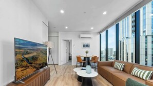 A modern living room with a large flat-screen TV, a sofa, a coffee table, and a dining area with chairs. - CBD VTA Apartment | Free Parking | Walk Everywhere (Adelaide)