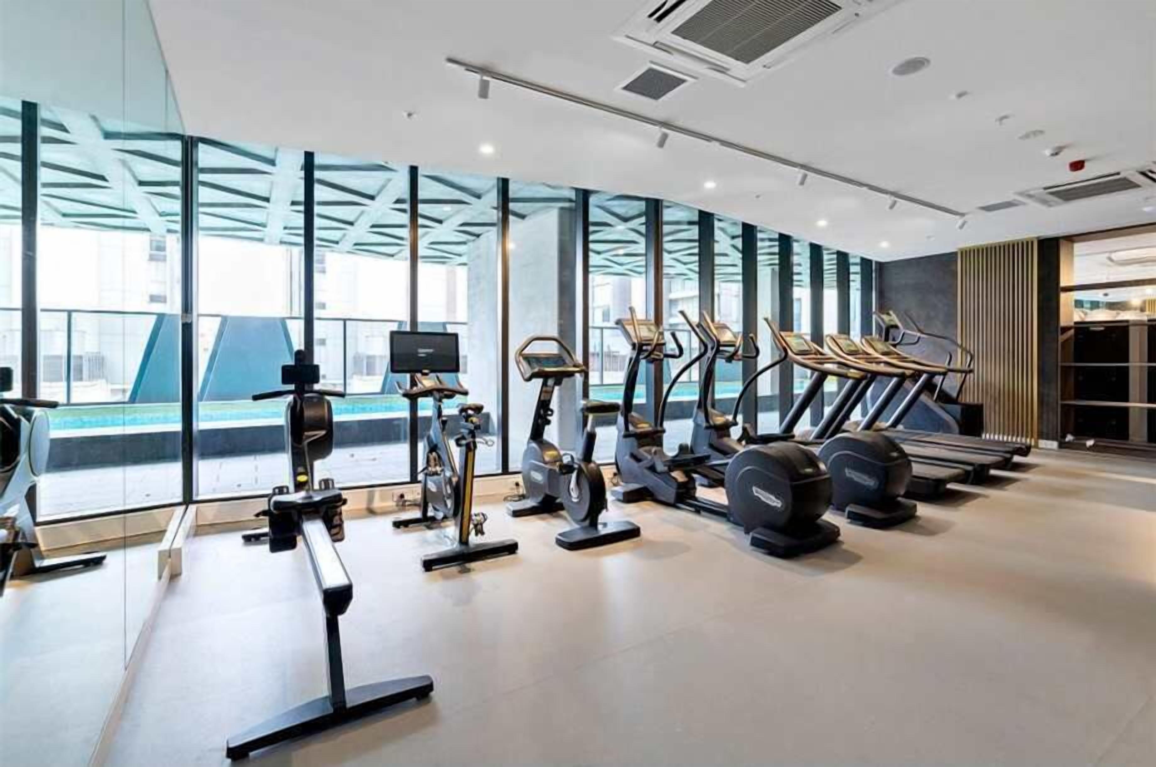 Un gimnasio moderno con diversos equipos de ejercicio, ventanas amplias y vista a la ciudad.