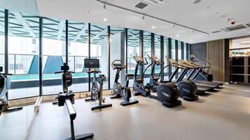 Un gimnasio moderno con diversos equipos de ejercicio, ventanas amplias y vista a la ciudad.