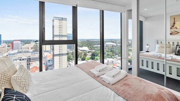 Una habitación de hotel moderna con una cama grande, vistas de la ciudad y un balcón con zona de estar.