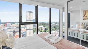 Una habitación de hotel moderna con una cama grande, vistas de la ciudad y un balcón con zona de estar.
