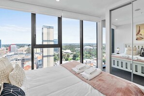 Une chambre d’hôtel moderne dotée d’un grand lit, offrant une vue sur le paysage urbain et comprenant un balcon avec un espace salon.