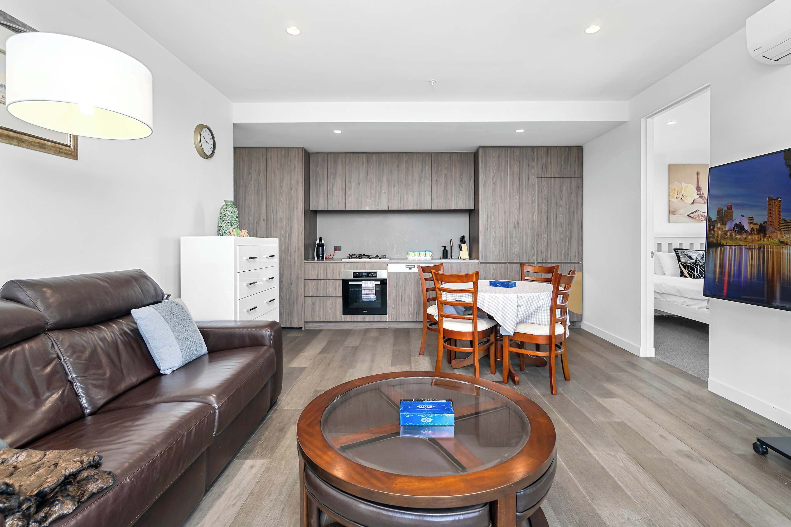 Una sala de estar moderna con un sofá de cuero marrón, una mesa de centro de vidrio y un comedor con sillas y una mesa de madera.
