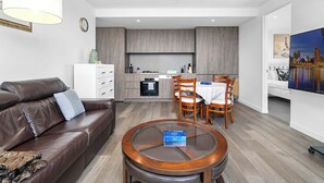 Una sala de estar moderna con un sofá de cuero marrón, una mesa de centro de vidrio y un comedor con sillas y una mesa de madera.