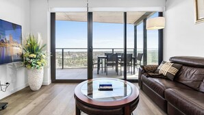 Una sala de estar moderna con una mesa de centro de vidrio, un sofá de cuero marrón y una planta grande en maceta.