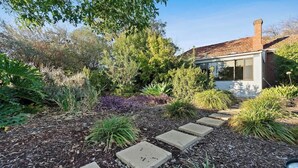 Un jardin avec un sentier menant à une maison dont le toit et la cheminée sont en briques.