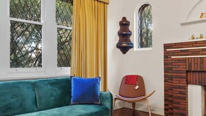 Une pièce avec un canapé vert, une chaise en bois, une cheminée et une fenêtre ornée de rideaux jaunes.