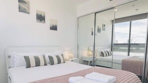 Una habitación de hotel moderna con una cama grande, un armario con espejo y una obra de arte en la pared.