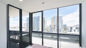 Un dormitorio moderno con una cama grande, un escritorio pequeño y un balcón con vista a la ciudad.