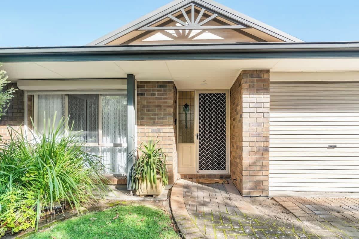 Una casa residencial con garaje, un porche cubierto y un pequeño jardín delantero con plantas.