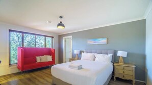 Un dormitorio con una cama grande, un sofá rojo, una mesita de noche con una lámpara y una ventana con vistas a árboles.
