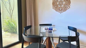 Un espace repas moderne avec une table en verre et des chaises noires, un élément d écoratif mural et une vue sur la verdure grâce à une porte coulissante.